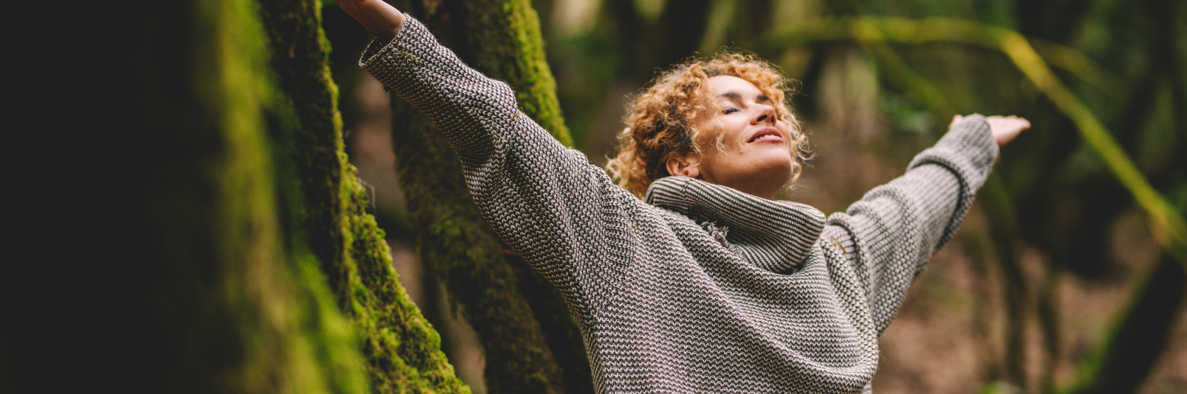Kvinde med udstrakte arme og lukkede arme i en skov