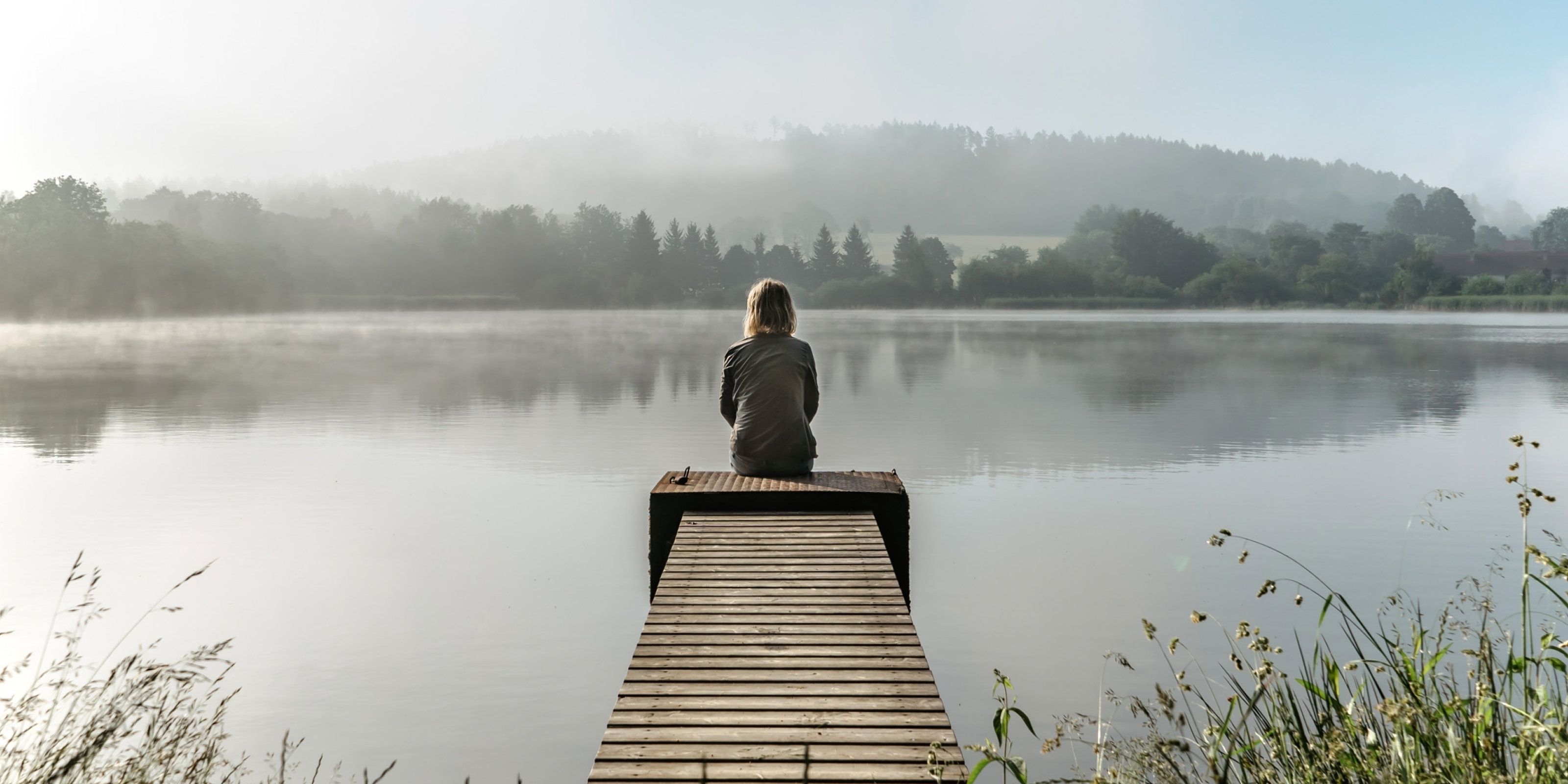 Kvinde sidder på en badebro og kigger ud over vandet